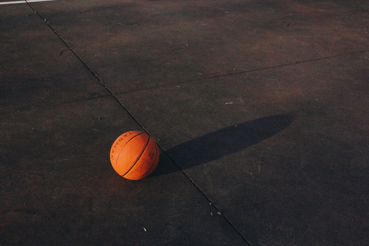 Basketball resting on a dark outdoor court at dusk