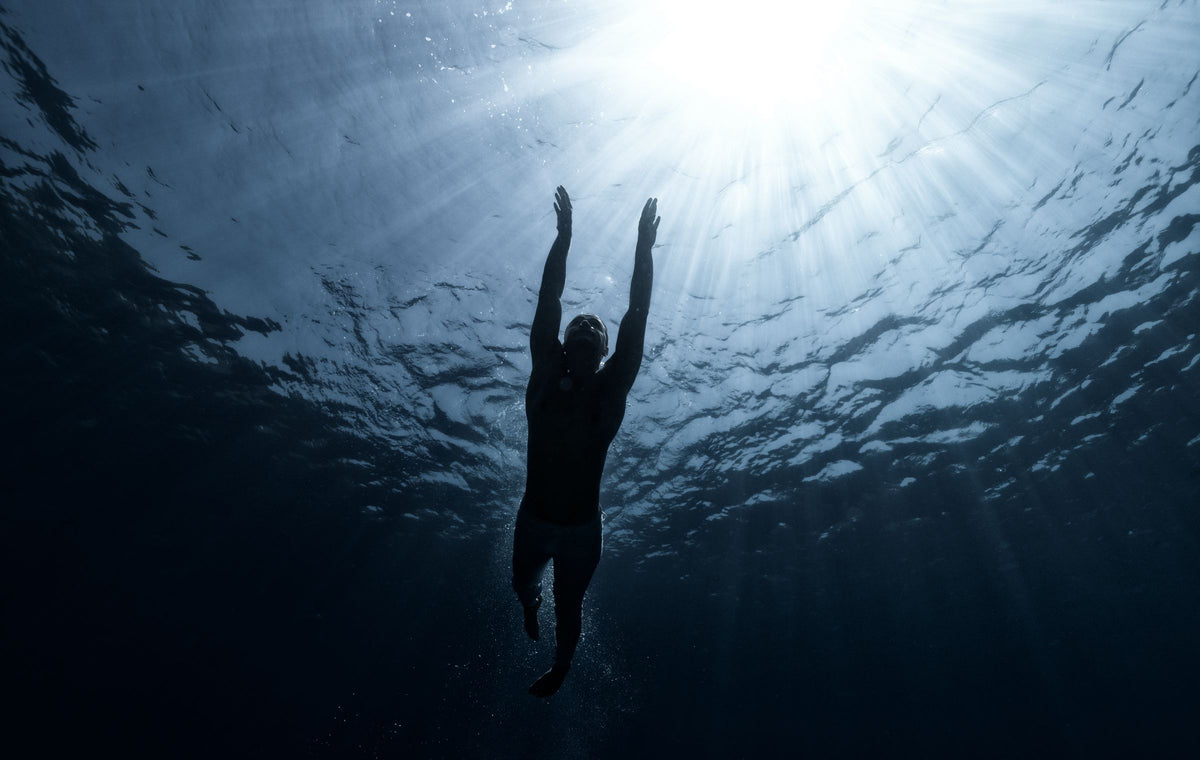 Silhouette of a swimmer underwater reaching toward the light
