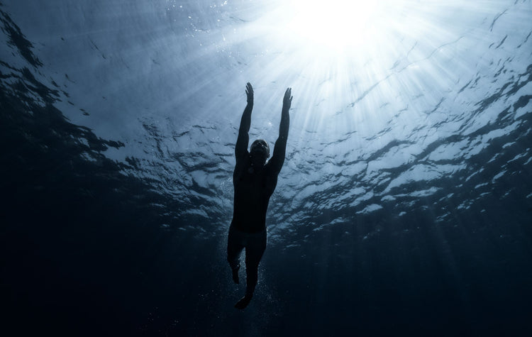 Silhouette of a swimmer underwater reaching toward the light
