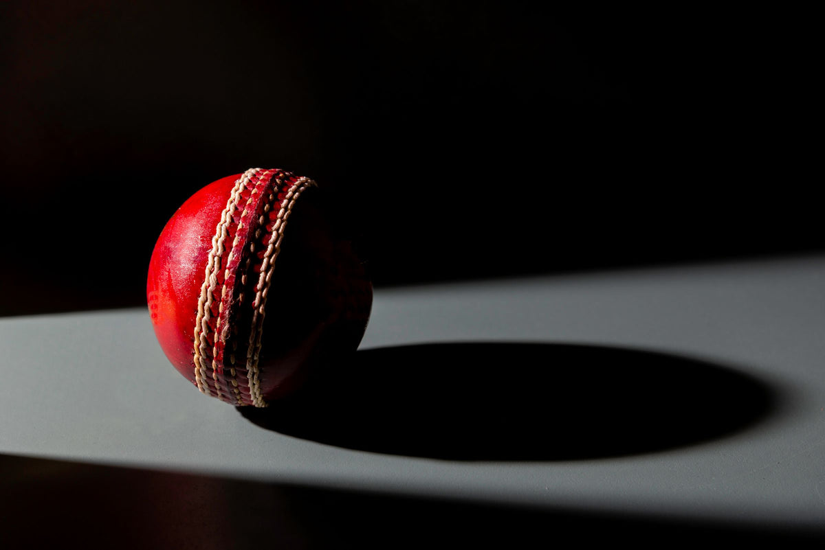 Red leather cricket ball casting a long shadow in low light